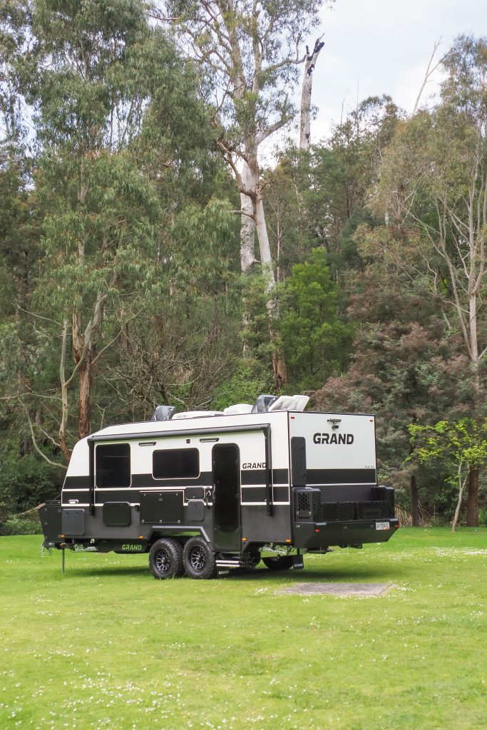 A Grand Caravan parked on the grass in front of an Australian woodland