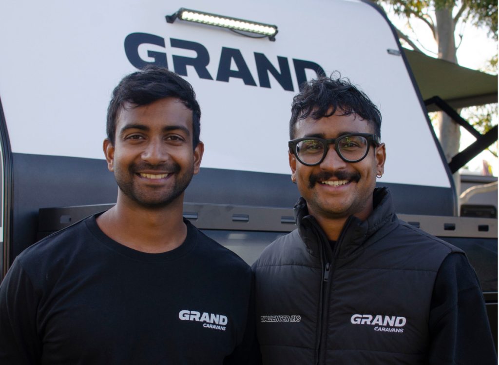 Two Grand Caravans employees smiling while stood in front of a Grand Caravan
